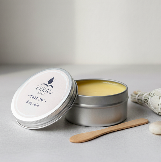 Feral Tallow balm in a metal tin with a wooden applicator on a neutral background
